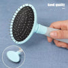 A hand holds a light blue pet grooming brush with black bristles against a gray fabric background.