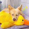 A golden retriever puppy rests its head on a yellow knitted plush toy shaped like a duck.