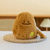 A fluffy brown plush vegetable doll resembling a peanut, resting on a woven mat.