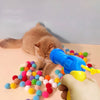 A hand is holding a blue toy gun that is firing colorful soft plush balls toward a cat.