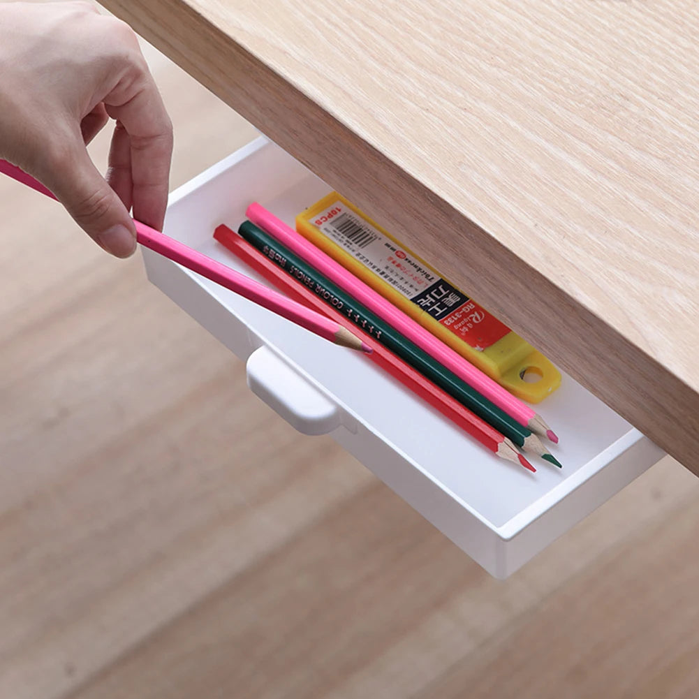 A hand places colored pencils into a white organizer tray inside a wooden desk drawer.