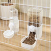 A clear automatic pet feeder containing dry food is visible inside a white dispenser, set within a wire cage.
