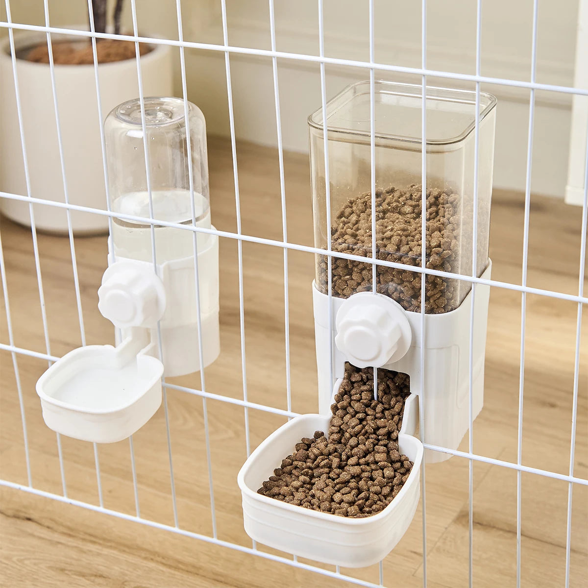 A clear automatic pet feeder containing dry food is visible inside a white dispenser, set within a wire cage.