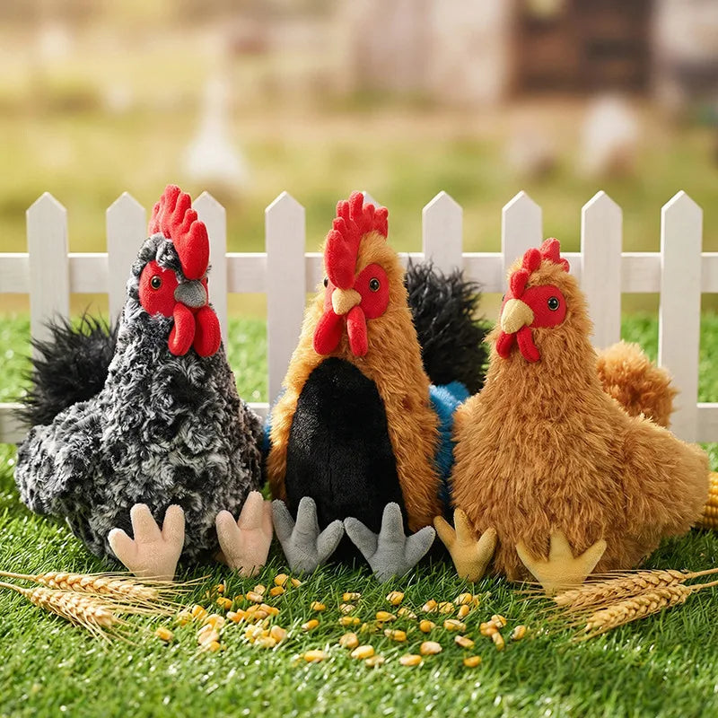A set of lifelike plush rooster and hen toys sitting on green grass behind a white picket fence.