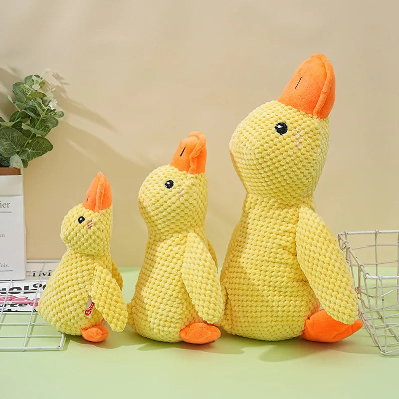 A yellow knitted plush duck toy with orange beak and feet sitting on a light green surface.