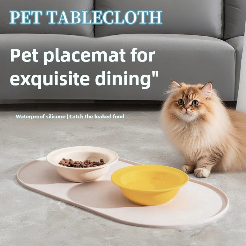 A cat is sitting next to a pink feeding mat with a yellow bowl on a gray surface.