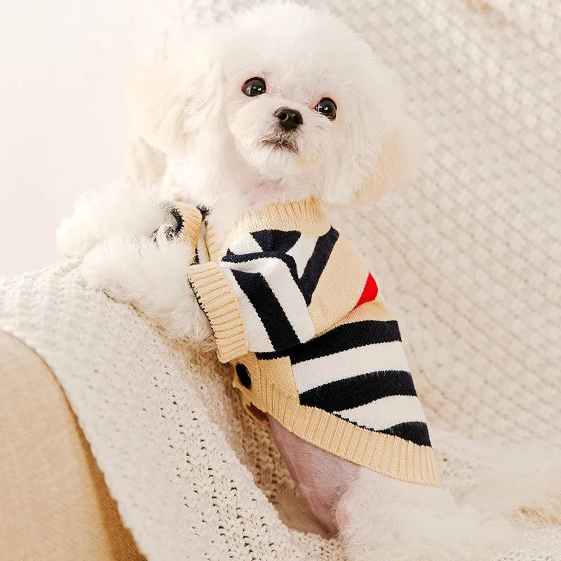 A fluffy white dog wearing a beige and black plaid knit sweater.