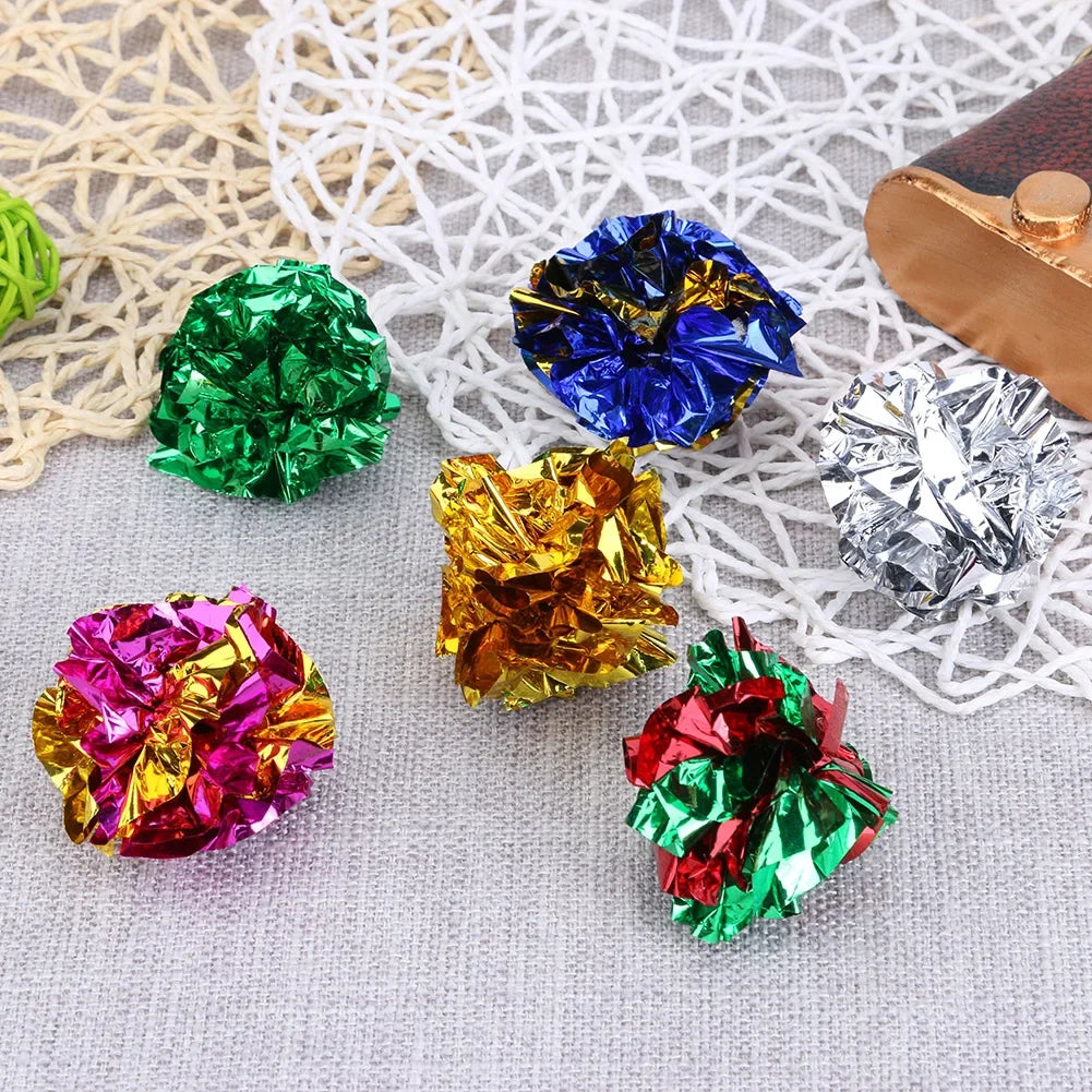 A collection of colorful crinkle balls in various shades including green, blue, gold, silver, and pink resting on a white mes