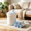 A white plastic trash bag with a blue drawstring top is placed on a beige rug next to a sofa.