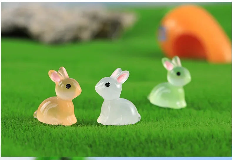 Two glow-in-the-dark resin bunny figurines, one yellow and one white, resting on green grass.