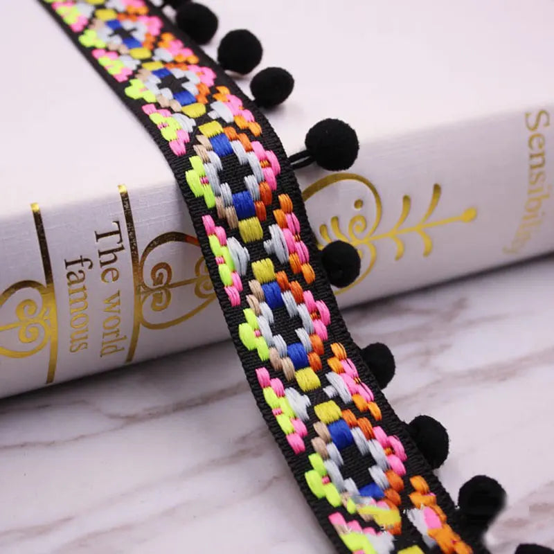 Close-up of a black lace trim with colorful mini pearl pom pom fringe for sewing and DIY crafts