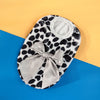 A black and white spotted knit pet sweater with a light gray bow displayed on a blue background.