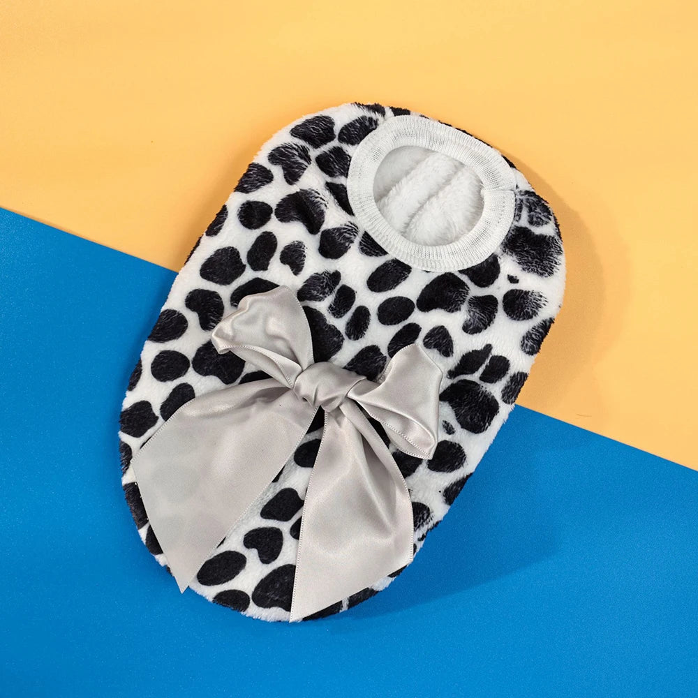 A black and white spotted knit pet sweater with a light gray bow displayed on a blue background.