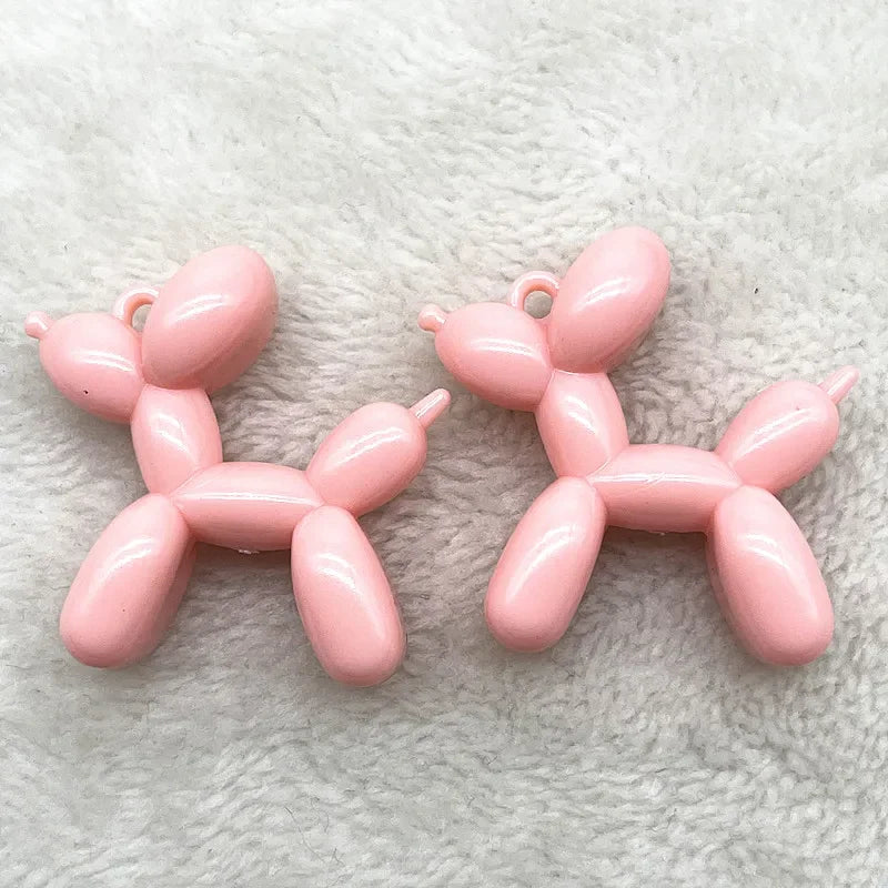 Two pink acrylic balloon dog charm pendants resting on a white fluffy surface.