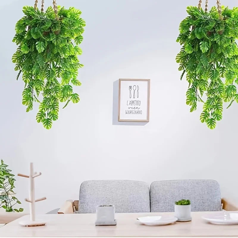 Künstliches Monstera-Blatt-Girlande hängt an einer weißen Wand über einem Holztisch.