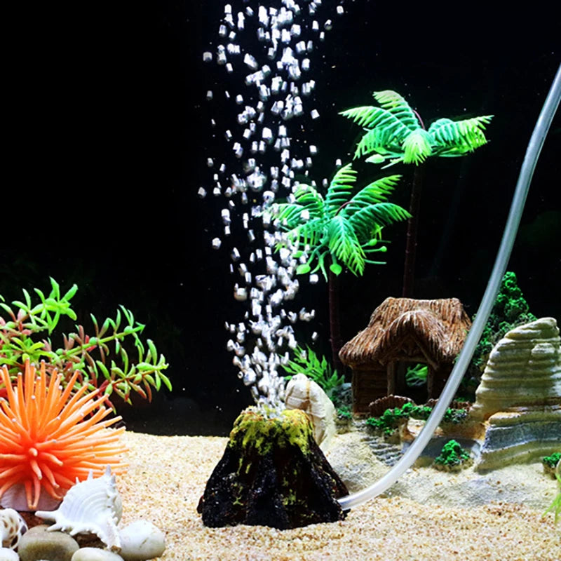 Aquarium decor featuring a simulated volcano, bubble stone, and an oxygenation tube with green aquatic plants.