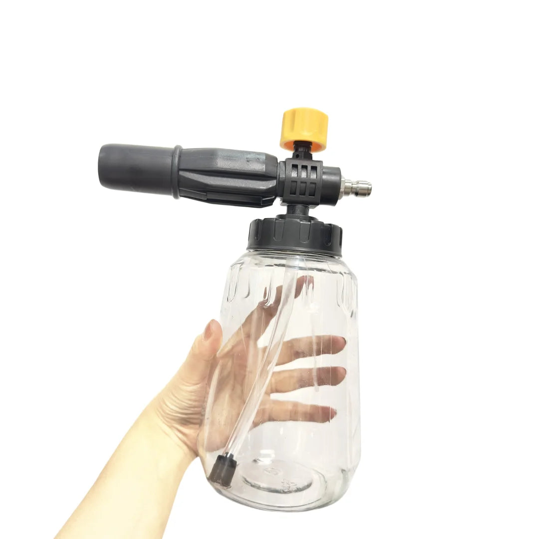 A hand holds a clear plastic bottle attached to a heavy-duty foam cannon with a yellow nozzle.
