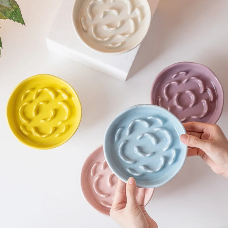 A hand holds a light blue ceramic slow feeder pet bowl with raised neck design, surrounded by other colored bowls.
