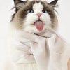 A fluffy cat with blue eyes and white fur is sticking out its tongue while wearing a light-colored pet cleaning wipe glove.