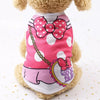 Un chien duveteux portant un gilet rose et blanc à motifs avec un grand nœud et des accents violets.