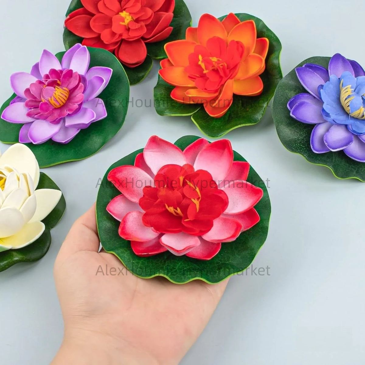 A hand holds a set of seven floating foam lotus flowers with green water lily pads in various colors.