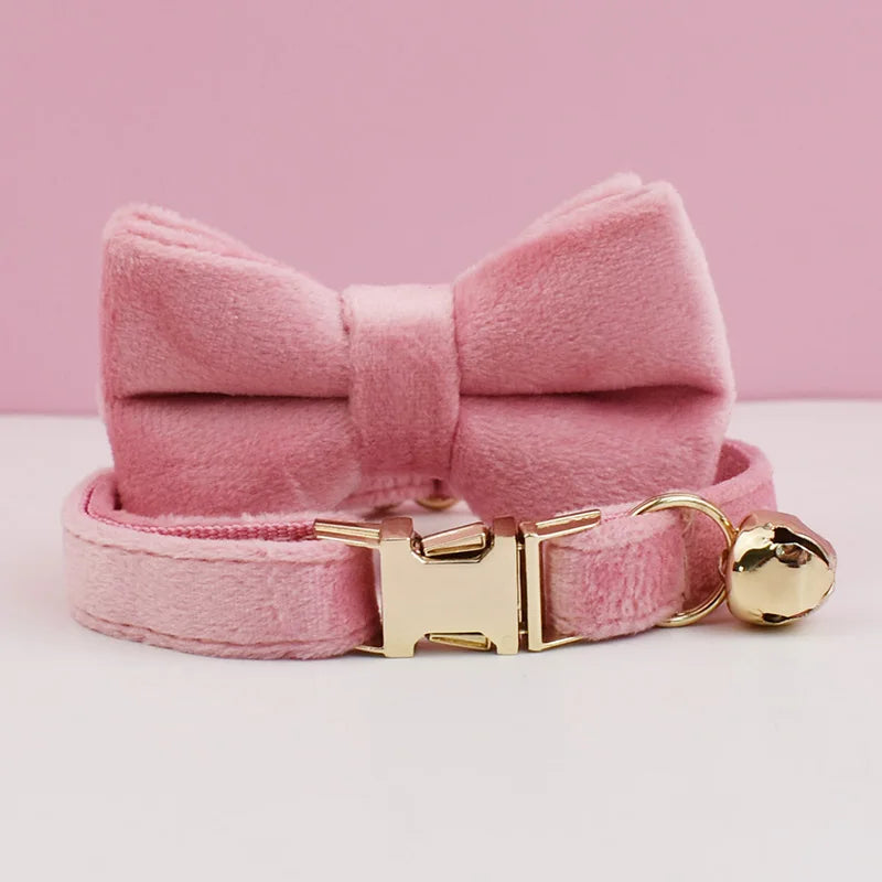 A pink velvet cat collar with a bow and a gold-tone buckle and bell.