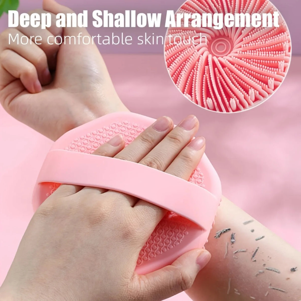 Hands are using a pink silicone exfoliating brush to gently scrub the skin.
