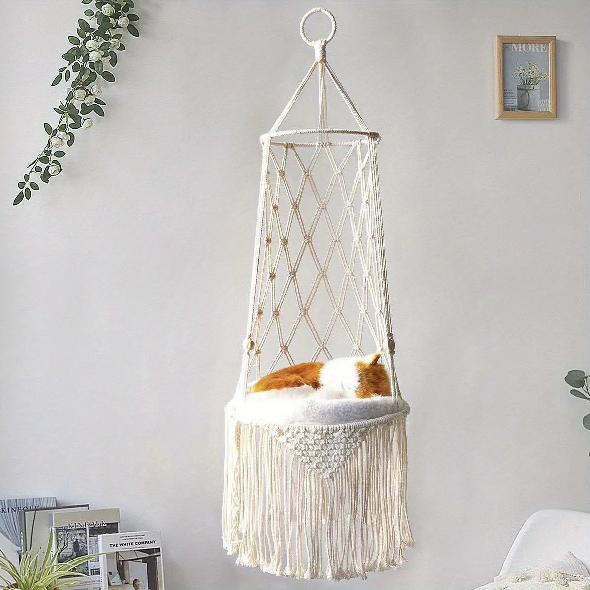 A white macrame cat hammock bed with soft fur resting inside, hanging on a wall.