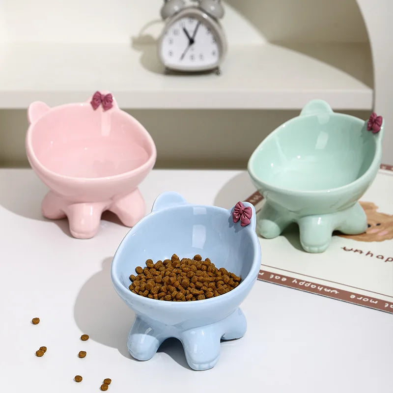 A set of three ceramic cat food bowls in pink, mint green, and light blue with raised tilted designs.