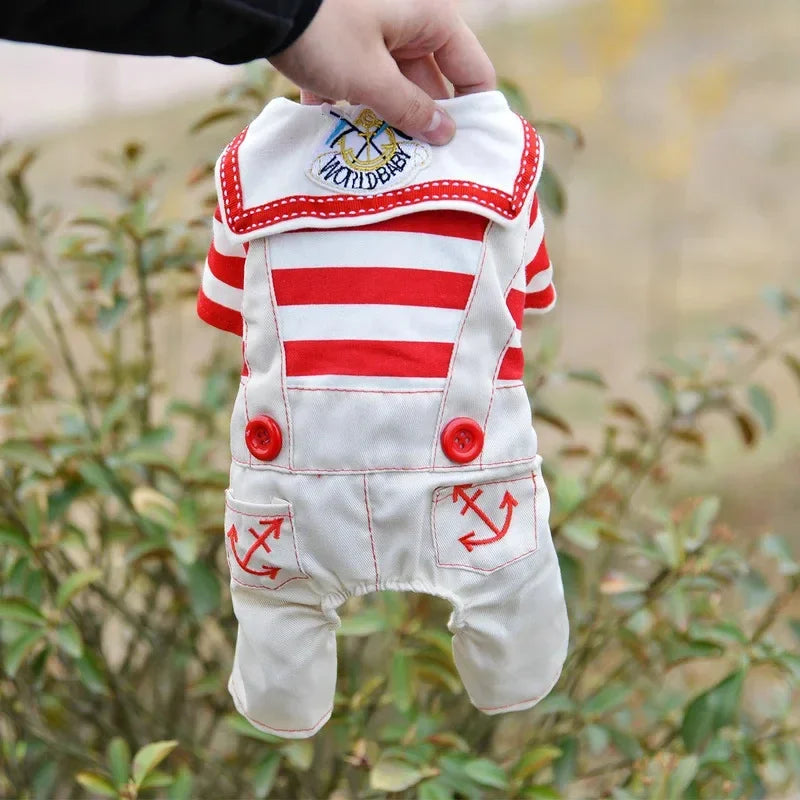 A white sailor dog costume jumpsuit with red stripes and nautical details being held by a hand outdoors.