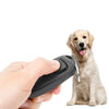 A hand holds a black dog training clicker and whistle with a key ring next to a golden retriever.