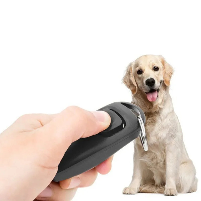 A hand holds a black dog training clicker and whistle with a key ring next to a golden retriever.