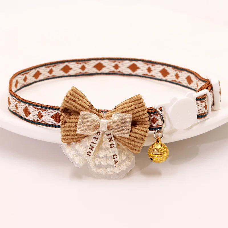 Breakaway cat collar featuring a woven patterned strap, a bowknot made of beige yarn, and a gold bell charm.