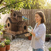 A woman is holding a rustic wooden bird house for garden decor outdoors.