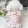 A pink floral print pet vest for dogs and cats with white lace trim and a fluffy white pom-pom collar.