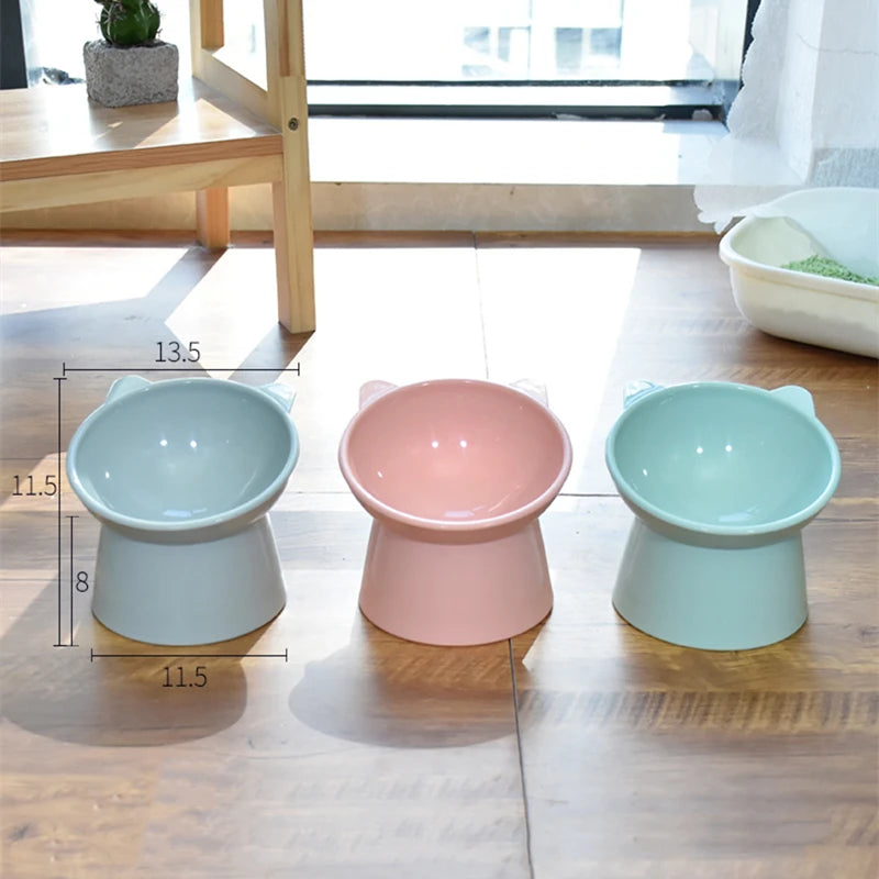 Three ceramic pet bowls in varying shades of pink and mint green sitting on a wooden table.