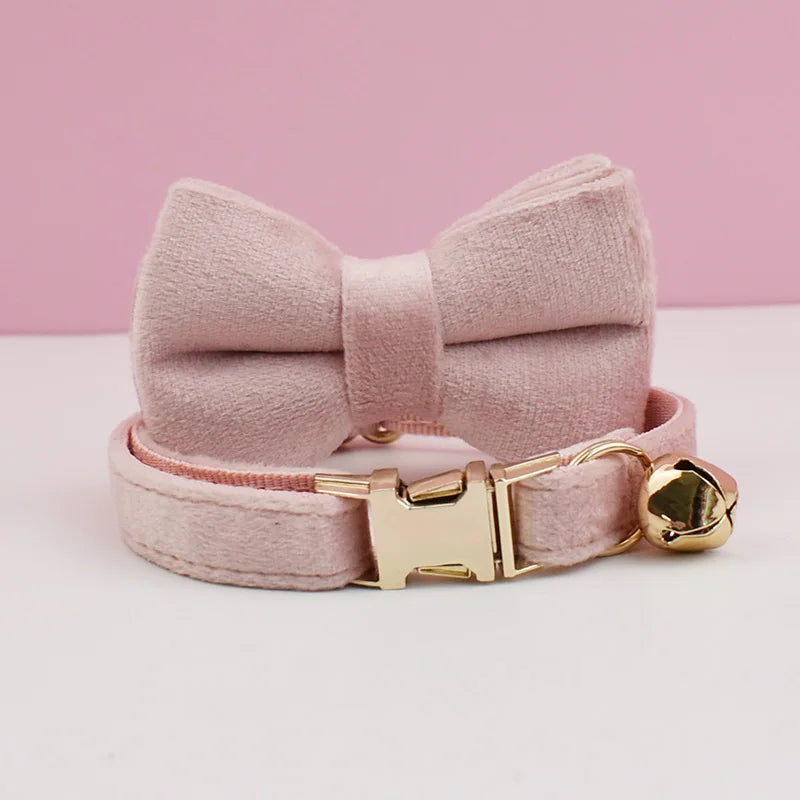 A pink velvet cat collar with a bow and a gold-tone buckle and bell.