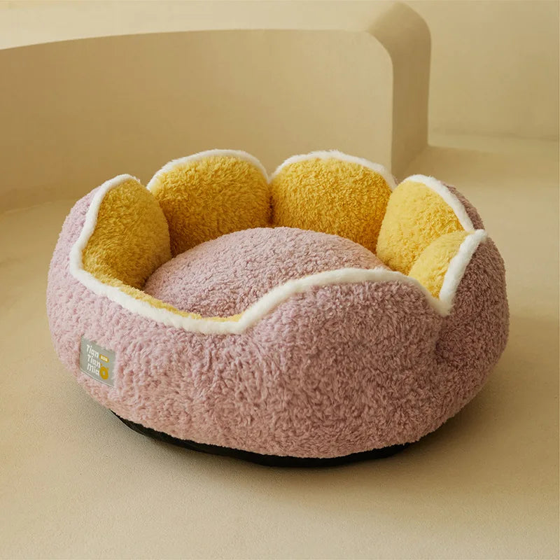 Rundes, rosa Plüsch-Katzennestbett mit gelben flauschigen Akzenten auf einer hellen Oberfläche.