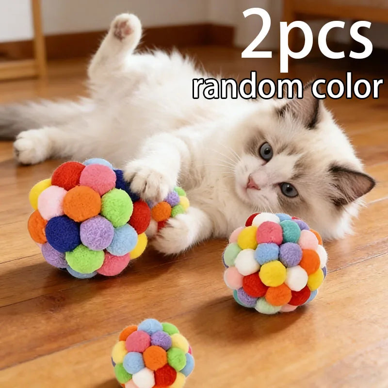 Two random color jingle bell cat toys are shown next to a white kitten.