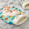 A fluffy orange and white kitten is relaxing inside a cozy plush sleeping bag with a tunnel hideaway on a gray surface.