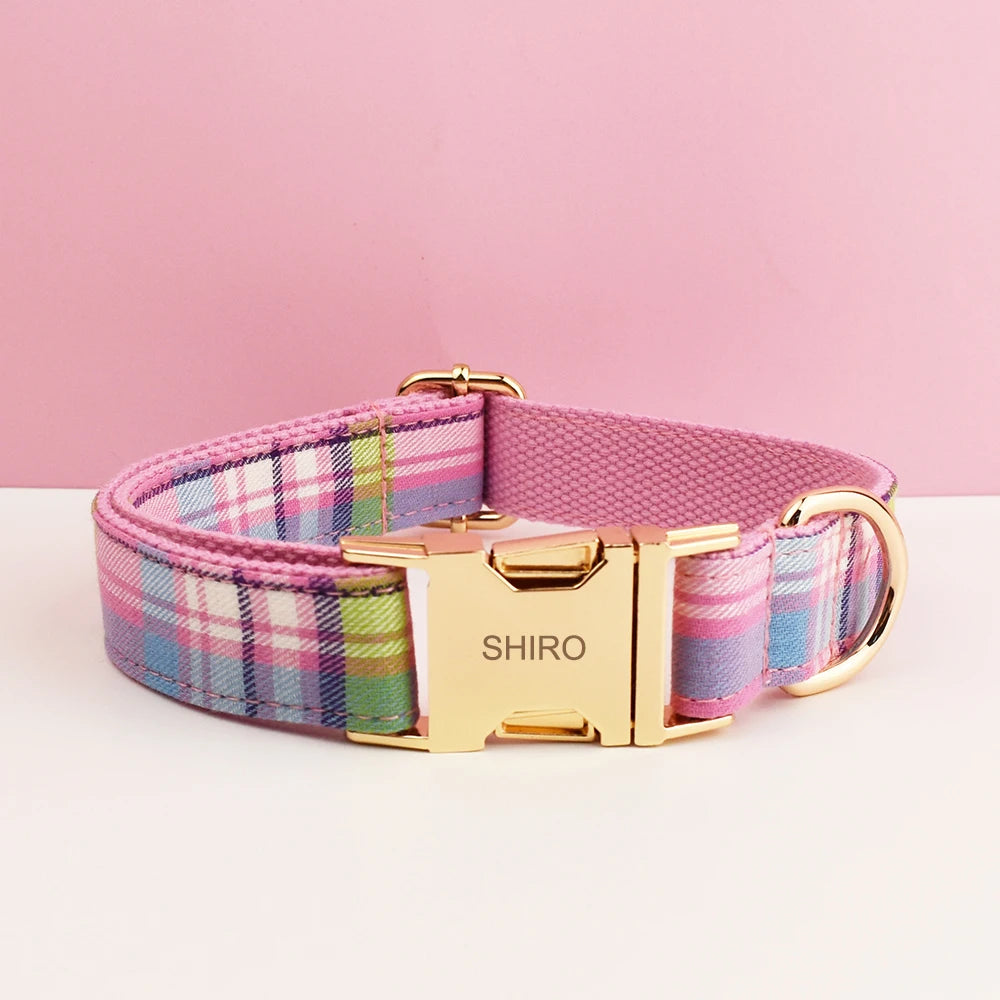 A pink plaid dog collar with a gold buckle and silver hardware is displayed on a white surface.