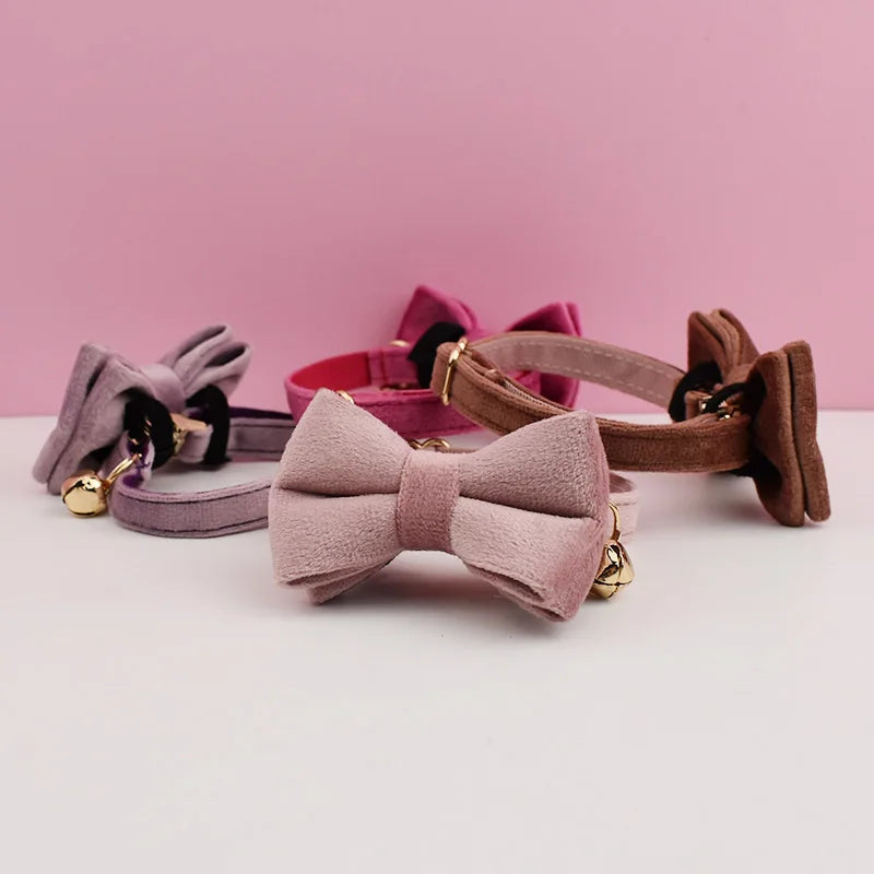 A collection of velvet cat collars in pink and mauve shades with black hardware displayed on a white surface.