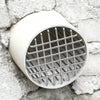 A round, white roof and floor drain mesh cover made of stainless steel, set against a rough stone wall.