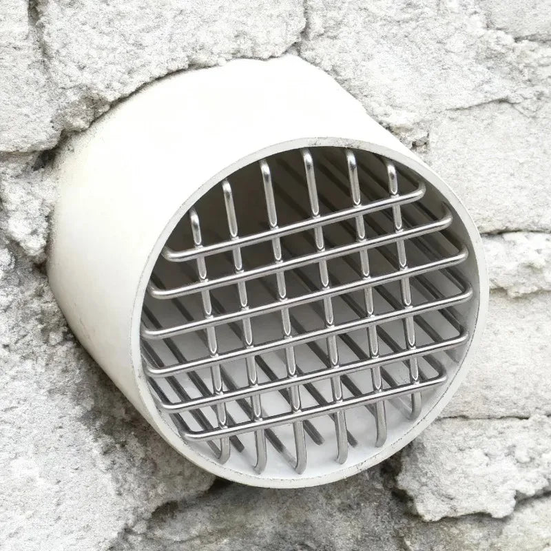 A round, white roof and floor drain mesh cover made of stainless steel, set against a rough stone wall.