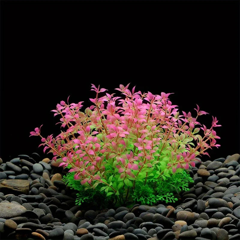A cluster of artificial aquarium plants with pink and green foliage growing in dark pebbles.