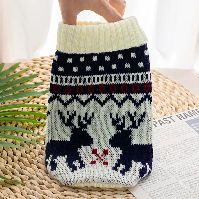 A knitted dog sweater featuring a festive pattern of deer and foliage in white, navy blue, and red yarn.