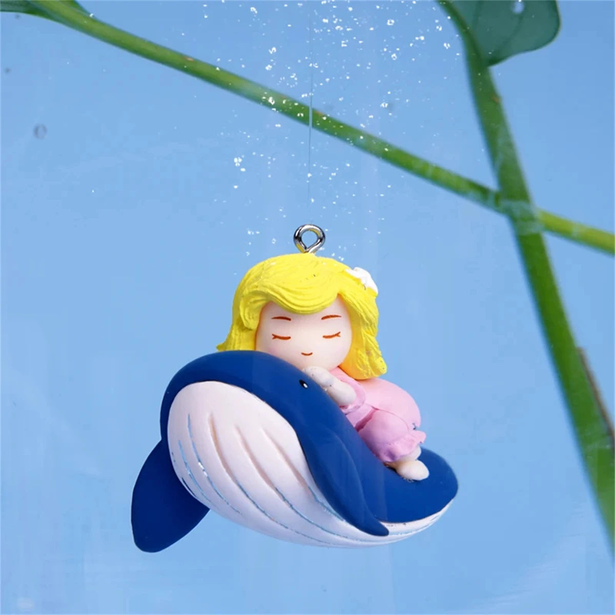 A yellow mermaid ornament with a pink tail is suspended by a transparent line against a blue sky.
