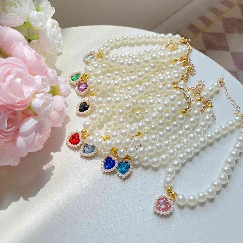 A delicate faux pearl necklace featuring a heart pendant and colorful gemstone accents, displayed on a white surface.