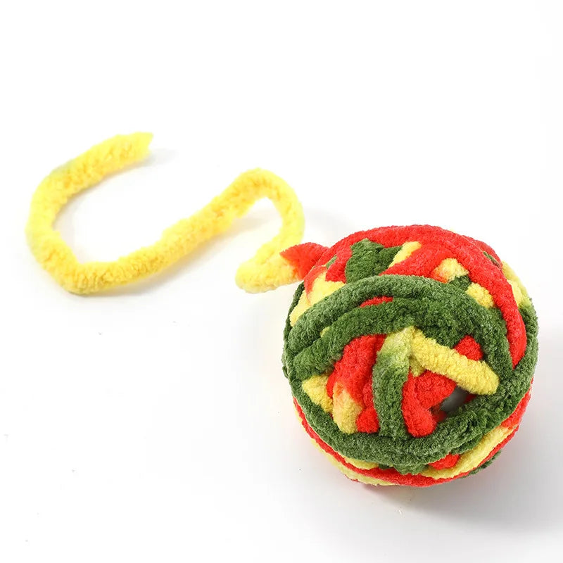 A soft plush cat toy ball with a bell, featuring vibrant red, green, and yellow textured fabric.