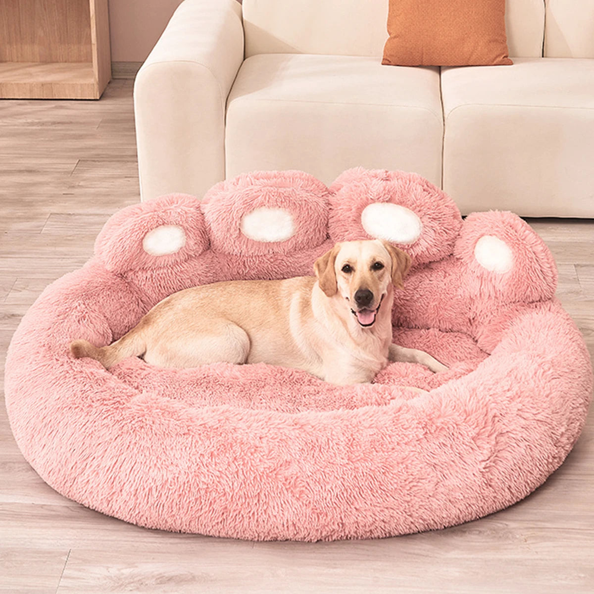 A light-colored dog is lying on a pink plush fluffy dog bed with rounded edges.